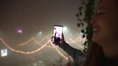 Elinde köpüklü şampanya kadehiyle mutlu bir kadın ailesiyle veya arkadaşlarıyla görüntülü görüşme yapıyor ve tezahürat yapıyor. Akıllı telefonlu bir kadın, harika bir şenlik geçmişi olan, dans eden bir kadın.