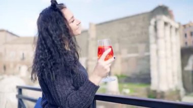 Roma mimarisinin panoramik manzarasından hoşlanan karizmatik manken, elinde bir bardak taze kokteyl ve renkli alışveriş torbaları tutan esmer kadın, ziyaretçi bayan