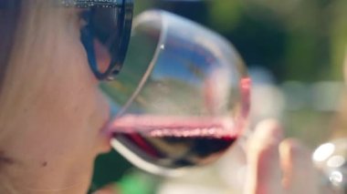 Attractive blonde woman tasting aged red wine in crystal glass at the open air party, pretty lady drinking high quality red wine dinning in rustic restaurant near the vineyard, shoulder shot of woman