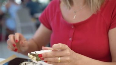 Attractive blonde woman tasting fresh open oysters in open air mediterranean restaurant, traditional seafood restaurants menu, expensive appetizers served on tray with ice and lemon slices. Person