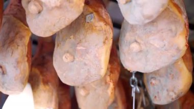 Delicious Italian cured prosciutto called Parma hanging on ceiling in local grocery store, traditional Italian seasonal meat product on market counter, famous jamon legs with salt and aroma spices