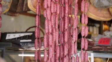 Dried rustic sausages and cured jamon legs in local Italian grocery store, variety of rustic meat delicatessen on market counter, seasonal dried, cured and smoked meat products in local store