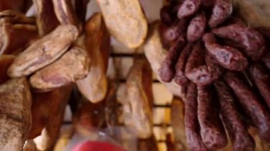Local Italian store with assortment of meat products hanging on ceiling, cred, smoked and dried ham, pork and sausages of rustic production, high quality Italian prosciutto legs and traditional smoked