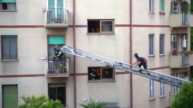 ROME, ITALY - AUGUST 27, 2021: Firefighters in working uniform and protective helmets lifting on rescue crane to buildings balcony to open the windows and enter apartment, rescue operation to save
