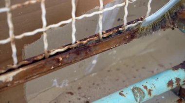 Process of removing rust and corrosion with special steel brush, worker in gloves rubbing upper faded layer of metal frame to remove rusty remnants, restoration and maintenance of steel surface