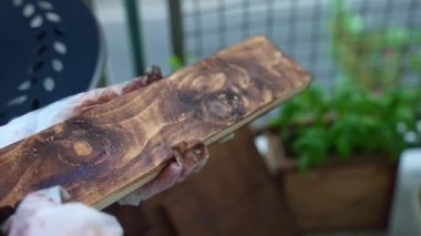 Carpenter coating wood plank surface with protective brown varnish using sponge, handyman restoring wood planks preparing for high-quality furniture production. High quality 4k footage