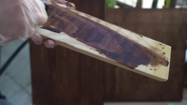 Man in gloves staining polished wooden plank with brown colour, joiner applying colour protection with sponge, staining wood surface texture, lacquer for improvement wooden conditions. High quality 4k