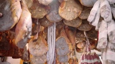 Local Italian grocery store with assortment of meat products, cured jamon leg, smoked ham and pork, and dried sausages hanging on ceiling, traditional Italian rustic food in local markets. High