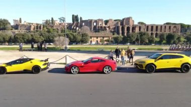 ROME, ITALY - NOVEMBER 7, 2022: Group of people talking against Fori Imperiali and parked exclusive sports cars background, yellow Lamborghini and red Ferrari on the side road in the centre of Rome