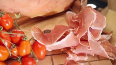 Tahta panoda geleneksel İtalyan antipasto, taze domates ve arka ışıklandırmada yüksek seçim jambonu dilimleri. Parmesan peyniri, İtalyan yemeği ve mutfak konseptiyle servis edilen lezzetli yağlı jamon.