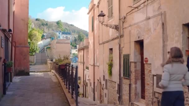 ヨーロッパの観光客は イタリアの小さな町や村の伝統的な狭い通りを楽しんで古い石畳の道に沿って歩いて アンティークの建物のファサードと田舎の中世の建築 ストック動画