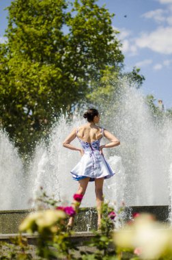 Kısa elbiseli kız arkası dönük fıskiyeye bakıyor.