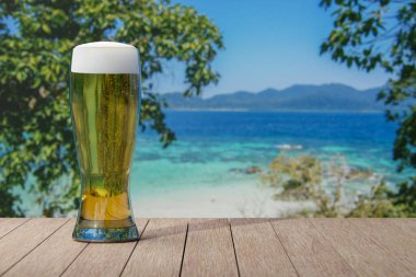 Masanın üzerinde turkuaz suyla deniz manzaralı bir bardak light bira..