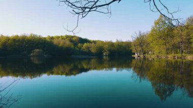 Trees and an old yellow house are reflected in the pond. Warm day in early spring, mirror lake with old houses