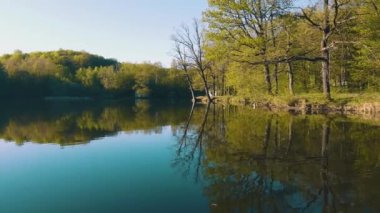 Trees and an old yellow house are reflected in the pond. Warm day in early spring, mirror lake with old houses