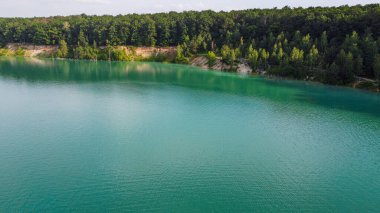 Aerial top-down flight over the amazing small lake of a perfectly round shape. Cloudy sky reflected in the clear turquoise water of a pond surrounded by trees and plants.