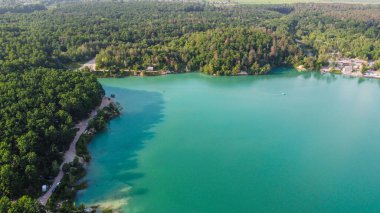 Aerial top-down flight over the amazing small lake of a perfectly round shape. Cloudy sky reflected in the clear turquoise water of a pond surrounded by trees and plants.