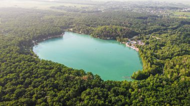 Aerial top-down flight over the amazing small lake of a perfectly round shape. Cloudy sky reflected in the clear turquoise water of a pond surrounded by trees and plants.