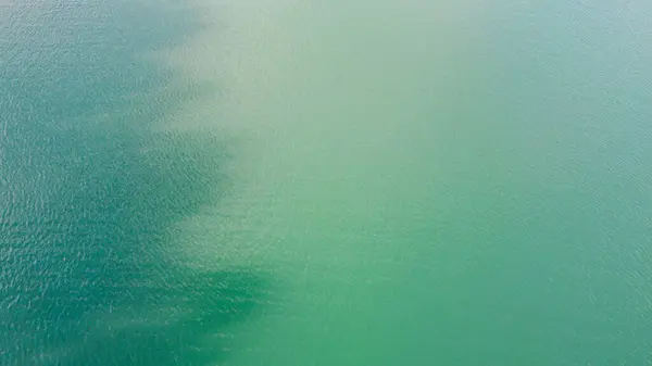Aerial top-down flight over the amazing small lake of a perfectly round shape. Cloudy sky reflected in the clear turquoise water of a pond surrounded by trees and plants.