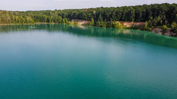 Aerial top-down flight over the amazing small lake of a perfectly round shape. Cloudy sky reflected in the clear turquoise water of a pond surrounded by trees and plants.