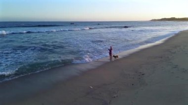 Beyaz kumsalın olduğu çarpıcı bir sahil. Bir kız yanında oyuncu köpeği ile balık tutmaya çalışıyor. Güneş ışıl ışıl parlıyor, plaj eğlencesi ve rahatlığı için mükemmel bir gün yaratıyor..