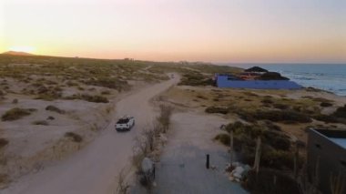 Beyaz bir kamyonet, San Lucas, Meksika kıyısındaki lüks evlerin yanındaki toprak yolda ilerliyor. Çarpıcı okyanus manzarası ve güzel mimari huzurlu bir sahil macerası yaratır..