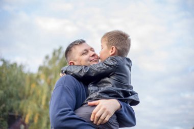 Mutlu baba ve oğul, yeşil doğada birlikte sarılıp oynuyorlar. Gölün ortasındaki küçük bir adada tahta bir yaya köprüsü olan balıkçı evi..