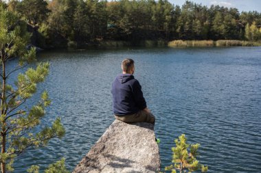 Kayada oturan adam, ormanın üzerindeki gölün manzarasının tadını çıkarıyor. Güzel bir sonbahar günü.