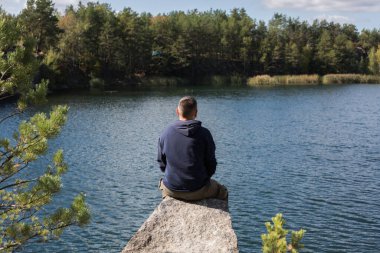 Kayada oturan adam, ormanın üzerindeki gölün manzarasının tadını çıkarıyor. Güzel bir sonbahar günü.
