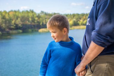 Baba oğluna sarılıyor ve baba oğul arasında eğleniyor. Mutlu, dişlek çocuk gülümsüyor. Sonbahar ormanı. Ebeveyn, çocuk. Dışarıda mutlu bir aile.
