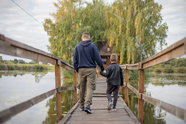 Happy father and son hugging and playing together in green nature. Fisherman\'s house with a wooden pedestrian bridge on a tiny island in the middle of the lake.