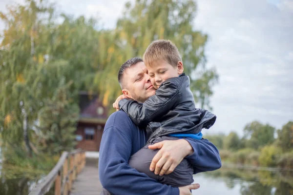 Happy father and son hugging and playing together in green nature. Fisherman's house with a wooden pedestrian bridge on a tiny island in the middle of the lake.