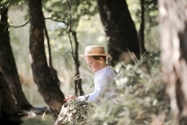 Bulanık yaz yeşilliği arka planında hasır şapkalı şişkin saçlı çocuğun portresi