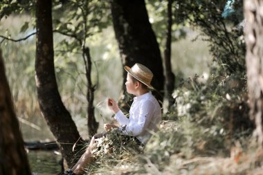Bulanık yaz yeşilliği arka planında hasır şapkalı şişkin saçlı çocuğun portresi