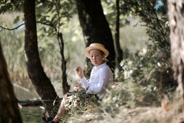 Bulanık yaz yeşilliği arka planında hasır şapkalı şişkin saçlı çocuğun portresi