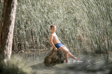 Yalnız çocuk Yunanistan 'daki yaz gölünün güzelliğine hayran. Dışarıda oynayan çocuk, gölde balık tutuyormuş gibi yapıyor..