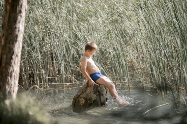 Yalnız çocuk Yunanistan 'daki yaz gölünün güzelliğine hayran. Dışarıda oynayan çocuk, gölde balık tutuyormuş gibi yapıyor..