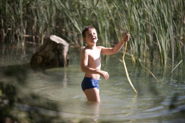 Yalnız çocuk Yunanistan 'daki yaz gölünün güzelliğine hayran. Dışarıda oynayan çocuk, gölde balık tutuyormuş gibi yapıyor..