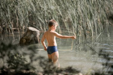 Yalnız çocuk Yunanistan 'daki yaz gölünün güzelliğine hayran. Dışarıda oynayan çocuk, gölde balık tutuyormuş gibi yapıyor..