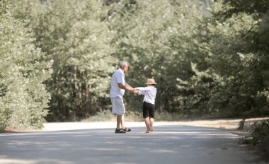 Büyükbaba ve torununun arka planda doğa yolunda yürüyen şapkaları var.