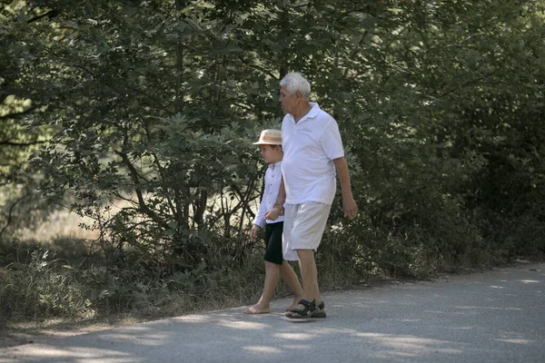 Büyükbaba ve torununun arka planda doğa yolunda yürüyen şapkaları var.