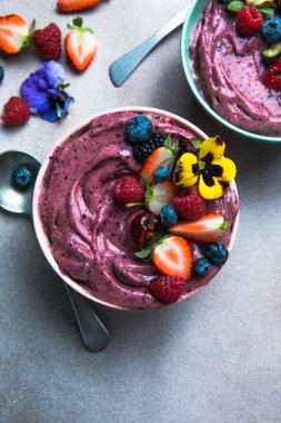 İki yaz acai smoothie kasesi. Çilekli, yaban mersinli, gri beton arka planda. Meyve ve gevrekli kahvaltı kasesi, yakın çekim, üst manzara, sağlıklı yemek.