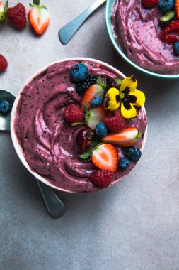 İki yaz acai smoothie kasesi. Çilekli, yaban mersinli, gri beton arka planda. Meyve ve gevrekli kahvaltı kasesi, yakın çekim, üst manzara, sağlıklı yemek.