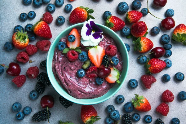 Two summer acai smoothie bowls with strawberries, blueberries,   on gray concrete background. Breakfast bowl with fruit and cereal, close-up, top view, healthy food
