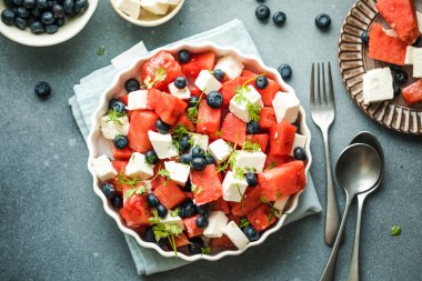 Karpuzlu yaz salatası, beyaz peynir ve gri arka planda yabanmersini. Vegan, Avrupa yemekleri.