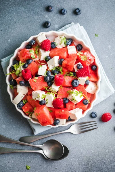 Karpuzlu yaz salatası, beyaz peynir ve gri arka planda yabanmersini. Vegan, Avrupa yemekleri.
