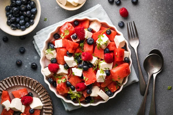 Karpuzlu yaz salatası, beyaz peynir ve gri arka planda yabanmersini. Vegan, Avrupa yemekleri.