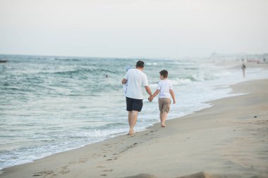 Baba ve çocuk gün batımında tropik plajda oynuyorlar. Deniz tatil beldesinde aile tatili. Babam güneşli bir akşamda çocuklarla okyanus kıyısında oynuyor. Çocuklarla seyahat et. Ebeveyn sevgisi