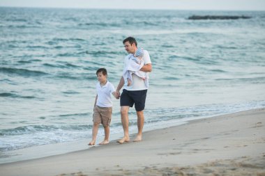 Baba ve çocuk gün batımında tropik plajda oynuyorlar. Deniz tatil beldesinde aile tatili. Babam güneşli bir akşamda çocuklarla okyanus kıyısında oynuyor. Çocuklarla seyahat et. Ebeveyn sevgisi