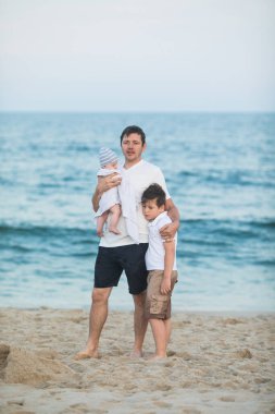 Baba ve çocuk gün batımında tropik plajda oynuyorlar. Deniz tatil beldesinde aile tatili. Babam güneşli bir akşamda çocuklarla okyanus kıyısında oynuyor. Çocuklarla seyahat et. Ebeveyn sevgisi